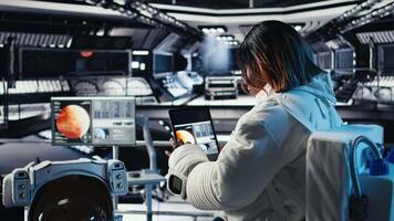 Astronaut inside futuristic spaceship checking red planet journey analytics during routine mission check. Space station cosmonaut using device, standing near monitor showing Mars expedition metrics video