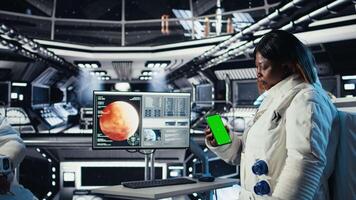 Astronaut using green screen smartphone to text friends before landing spaceship on Mars. Woman using chroma key phone to chat with family during mission to red planet surface in deep space, camera A video