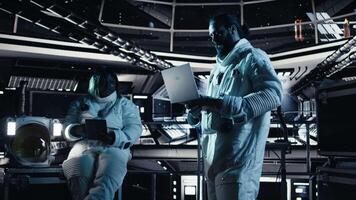 Astronaut studying star charts on laptop, discussing with colleague during space mission. Teamworking cosmonauts look at galaxy visualization on notebook during mankind survival expedition, camera A video