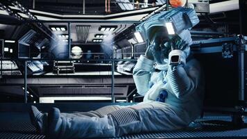 Unhappy cosmonaut sighs, having mental health affected by prolonged solitude. Depressed astronaut sits on orbit station floor in silence after weeks without contact in isolated space habitat, camera A video