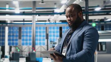 Black master engineer overseeing photovoltaics production line in a factory, ensuring a successful manufacturing process to meet corporate goals and alternative energy standards. Camera A. video