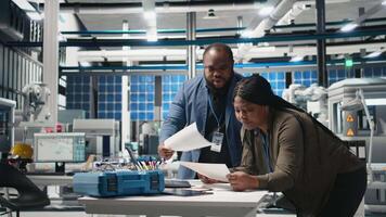 Team of african american consultants reviewing data and checklists in modern solar power facility, ensuring manufacturing process meets sustainable energy and innovation standards. Camera B. video