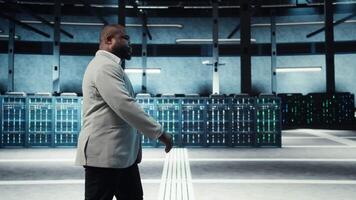 Employee walking in high tech data center with hardware used to host websites. IT professional overseeing dimly lit server farm setup helps companies stay connected, camera A video