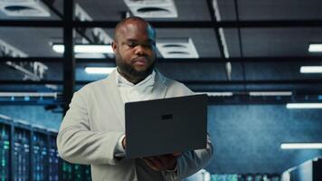 Engineer walking in data center using AI automation during maintenance session. African american server hub worker configuring deep learning models in hardware rigs, camera B video