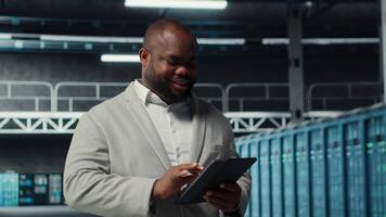 System administrator walking in server farm deploying infrastructure for efficient data analysis. Worker using device in dat a center in managing storage systems for datasets, camera B video