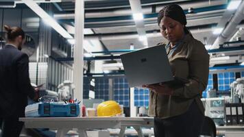 Woman master engineer examining production line for photovoltaics, reviewing manufacturing process data on laptop. Working on alternative energy success for industrial operations. Camera B. video