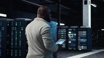 Software developer in data center using tablet, employing AI machine learning models. Employee using device to fulfill artificial intelligence infrastructure needs, allocating resources, camera A video
