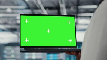 Close up of technician upgrading equipment in data center using isolated screen laptop. IT professional in high tech establishment overseeing server rows with chroma key notebook, camera B video
