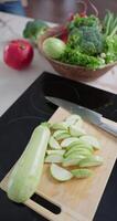 Vertical slow-motion footage of slices of sliced zucchini are on the cutting board on the kitchen table, a kitchen knife, plate with broccoli, green onion, red radish, lettuce, pomegranate video
