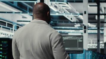 Programmers walking in data center coding, doing resource optimization using tablet. Server farm worker in data center refining algorithms for faster processing using device, camera B video