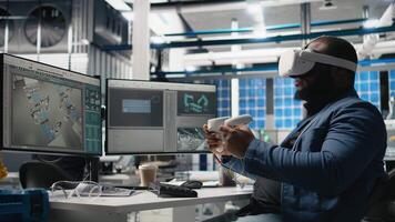 Black photovoltaics factory expert uses VR glasses to assembly digital solar cells, working with robotic arms for solar panels placement. Engineer uses machinery with virtual reality. Camera B. video