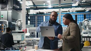 Black factory inspectors engaging in a briefing over the manufacturing process, reviewing production line and metrics on files. Supporting renewable energy improvement. Camera B. video