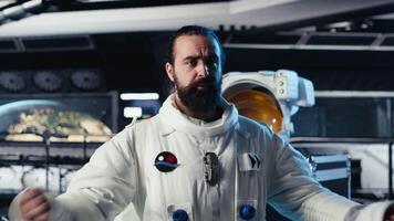 Astronaut waves hand, communicating with command center during videocall to share recent orbit discoveries. Cosmonaut salutes Earth team, provides scientific findings from spacecraft, camera B video