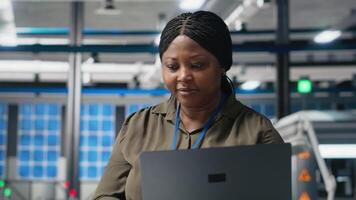 African american female expert reviewing solar panels production line, doing quality control in a photovoltaics factory. Analyzing data reports and insight to create solar power. Camera A. video