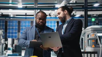 Multiethnic business associates and engineers gather for a discussion in a solar tech manufacturing facility, planning future developments in sustainable energy and industrial operations. Camera A. video