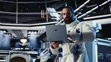 Astronaut reviewing onboard analytics on laptop before stepping out for scheduled operations outside space station. Cosmonaut verifying mission parameters after landing on alien planet, camera B video