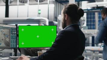 Young business specialist uses computer with green screen and production metrics, overseeing the industrial operations and high tech equipment. Master engineer works on sustainability. Camera A. video
