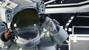 Cheerful astronaut holding helmet doing human expansion in space using spacecraft. Happy african american woman in starship prepares for expedition supporting long term mankind survival, camera B video