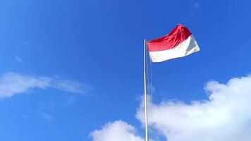 The Indonesian national flag flutters against a cloudy blue sky background from a low angle camera. The red and white flag. The Unitary State of the Republic of Indonesia. video
