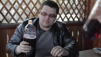 Two men sit at the table on terrace and drink beer from plastic bottles. Happy and satisfied. video