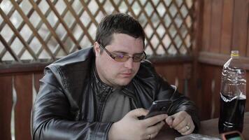 Men sit at the table on terrace and drink beer from plastic bottles and play on smartphone. Happy and satisfied video