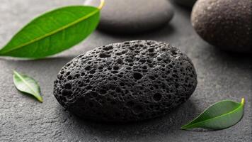 Black pumice stone with green leaves on grey background closeup. photo
