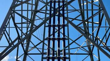 This image presents a detailed view of a high voltage transmission tower set against a clear blue sky background photo