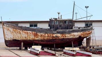 An old, weathered fishing boat, displaying visible signs of rust and decay, is currently resting in a dry dock area photo
