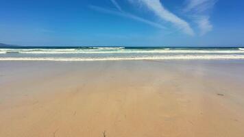 A serene and tranquil beach scene showcasing soft, warm sand, gentle waves lapping, and a clear blue sky above photo
