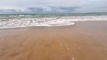 A beautifully serene view of gentle waves continuously lapping at a golden sandy beach beneath cloudy skies photo