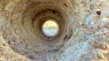 There is a captivating and breathtaking view framed by a circular rock tunnel, showcasing a stunning natural landscape photo