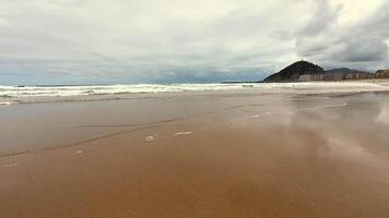 A peaceful beach scene depicting gentle waves softly lapping against the sandy shore beneath a cloudy sky photo