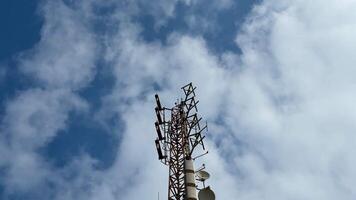 The image shows a telecom tower against a bright blue sky with fluffy clouds, highlighting its antennas photo