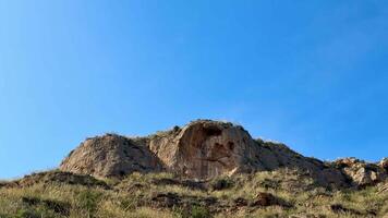 A breathtaking and stunning view of a unique rock formation surrounded by lush, vibrant grasslands beneath a clear sky photo