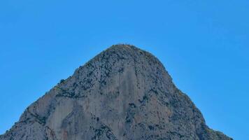 The breathtaking view of a rocky mountain peak rises beautifully against a vibrant and clear blue sky above photo
