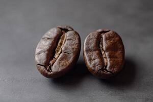 Two roasted coffee beans rest on a dark surface photo