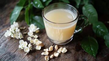 A glass of light colored beverage with white flowers and leaf photo