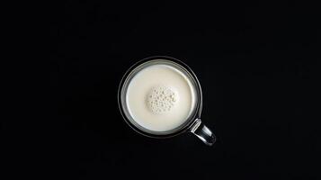 A glass mug filled with frothy milk sits on a black background photo