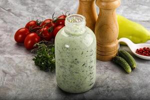 A bottle of dressing next to a pepper and a tomato photo