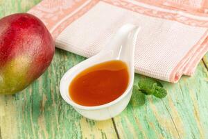 A spoon with a mango sauce and a spoon with a green leaf photo