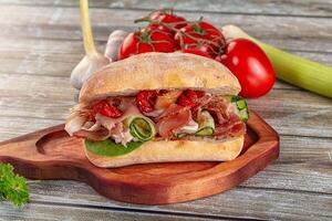 A sandwich with meat, vegetables and tomatoes on a wooden cutting board photo