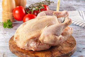 A chicken on a wooden cutting board with tomatoes and herbs photo