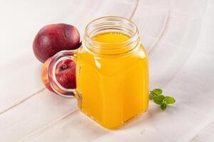 A glass jar with a glass of juice next to a peach photo