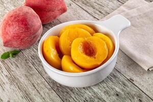 A bowl of sliced peaches on a wooden table photo
