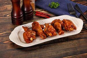 A plate of chicken wings on a table with a bottle of ketchup and a bottle of hot photo