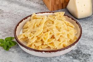 A bowl of pasta with cheese and basil on a table photo