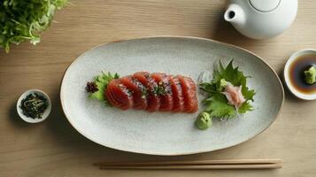 Oval plate of fresh tuna sashimi, garnished with sesame seeds, daikon radish, and wasabi. Served with soy sauce and a small side dish of pickled vegetables photo