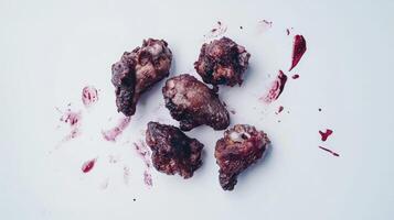 Darkened, roasted, poultry pieces, scattered on a white surface, with purple-red sauce splatter photo