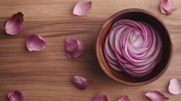 Thinly sliced red onion rings in a wooden bowl, surrounded by onion petals photo