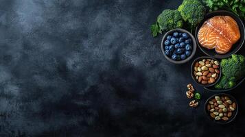 Healthy food arrangement on dark surface. Fresh salmon fillet, broccoli, blueberries, and nuts arranged at the top right corner of a dark, textured background photo